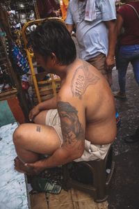 Rear view of shirtless man sitting on floor