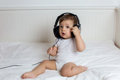 Baby boy in big headphones in white big bed