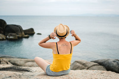 Man sitting on rock at sea shore against sky