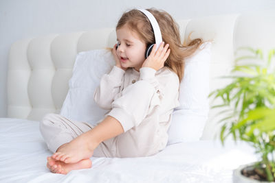 Cute girl listening music while sitting on bed