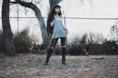 Full length of young woman with arms raised against trees