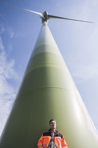 Engineer standing in front of tall wind turbine on sunny day