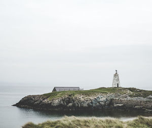 Lighthouse on rock by sea against sky