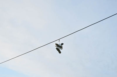 Low angle view of shoes hanging on cable against sky