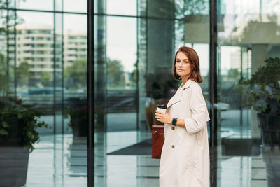 Portrait of young woman standing against window