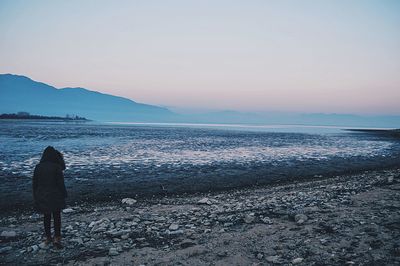 Rear view of person standing by lake kerkini against sky during sunset