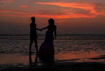 Silhouette couple standing on beach against orange sky