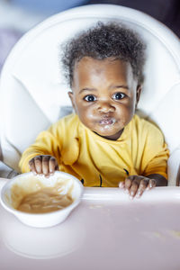 Cute girl child eating while sitting on high chair at home
