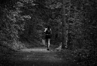 Woman running on footpath amidst trees in forest