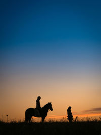 Silhouette people riding against sky during sunset