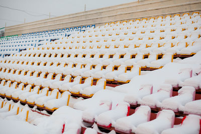 Empty outdoor football soccer stadium seats covered with snow in winter, light snowfall.