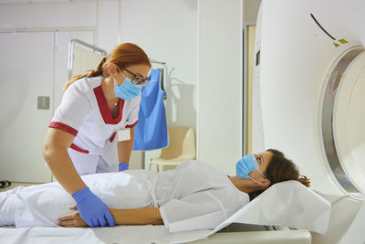 Doctor in uniform and eyeglasses using tomography machine with lying female patient in hospital