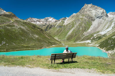 Rear view of man sitting on bench against mountains