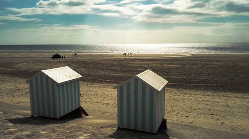 Huts at beach against sky on sunny day