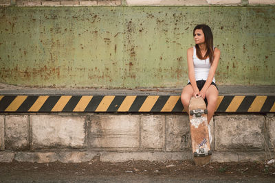 Young woman looking away while sitting against wall