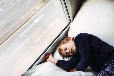 High angle view of boy sleeping on bed by window
