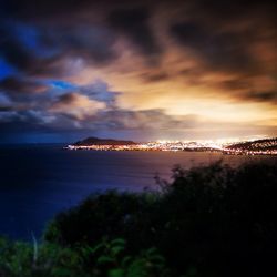 View of illuminated cityscape against cloudy sky