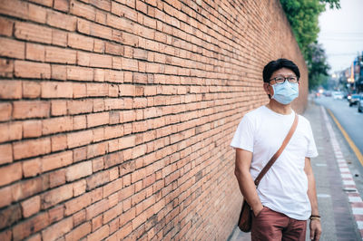 Man wearing mask standing against brick wall