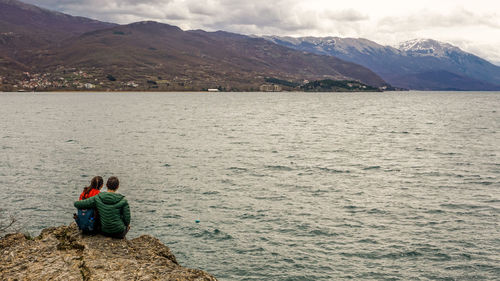 Rear view of women sitting by lake against mountains