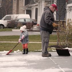Grandfather with granddaughter cleaning snow outdoors