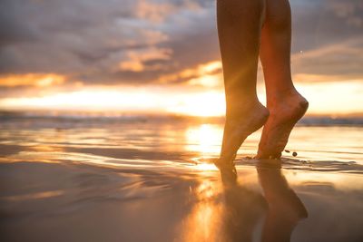 Low section of person standing on beach during sunset