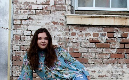 Portrait of young woman sitting against brick wall