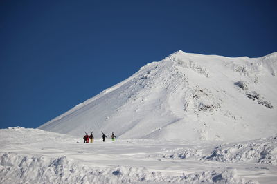 People on snowcapped mountain against clear blue sky