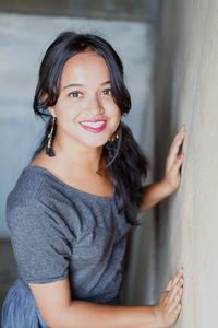Portrait of a smiling young woman standing against wall