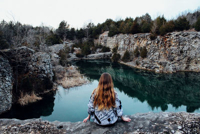 Woman sitting by lake against clear sky