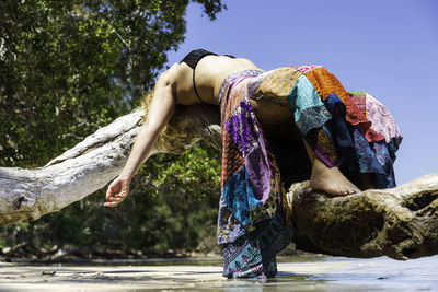 Full length of woman in bikini lying on fallen tree trunk by sea