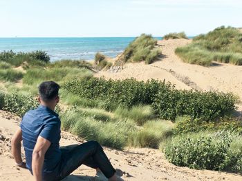 Man sitting on beach looking at sea against sky