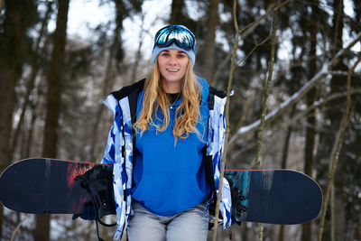 Portrait of young woman holding snowboard during winter