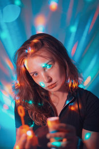 Portrait of young woman holding bubble wand against illuminated lights