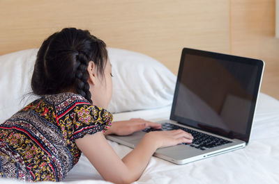 Girl using laptop while lying on bed at home