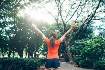 Rear view of woman with arms outstretched against plants