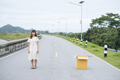 Portrait of young woman standing on road against sky