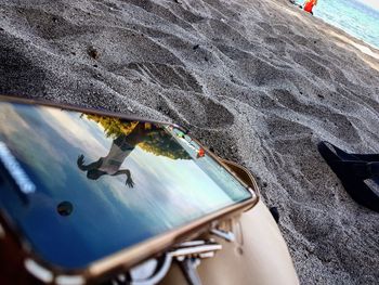 Reflection of woman on screen of mobile phone at sandy beach