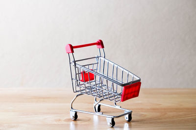 Close-up of shopping cart on wooden table against wall