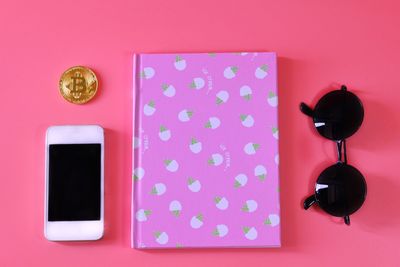 Directly above shot of pink diary with smart phone and sunglasses over colored background