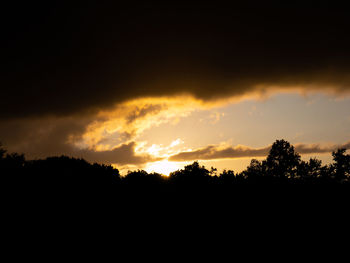 Silhouette trees against dramatic sky during sunset