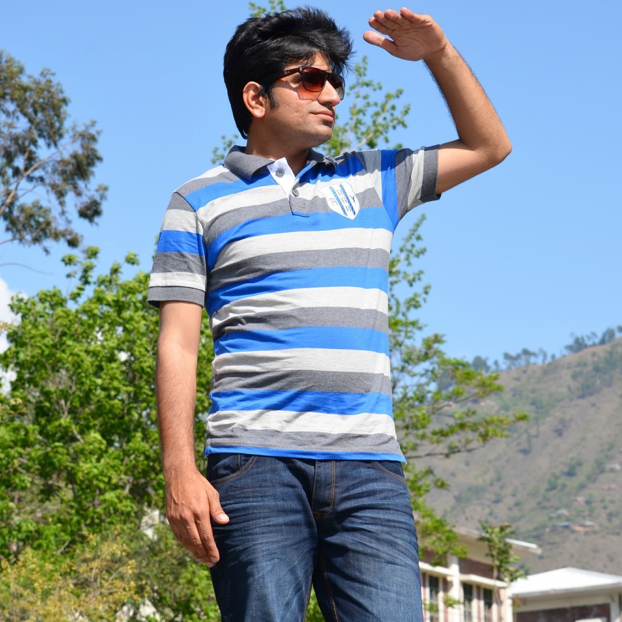 LOW ANGLE VIEW OF YOUNG MAN STANDING AGAINST CLEAR BLUE SKY