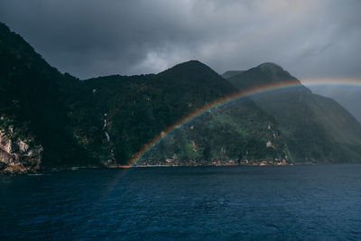 Scenic view of rainbow over sea and mountains