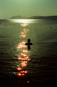 Silhouette woman standing in sea against sky during sunset