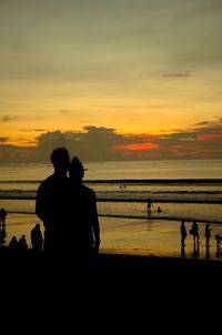 Silhouette people on beach against sky during sunset