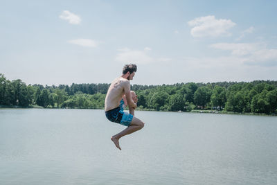 Full length of shirtless man diving in river against sky