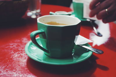 Close-up of coffee cup on table with hand in background