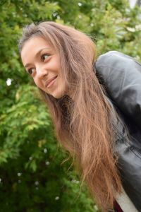 Low angle view of smiling young woman standing against trees at park