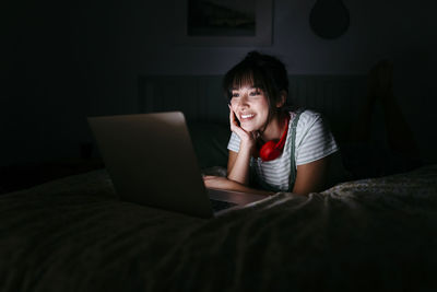 Portrait of smiling young woman using laptop on bed at home