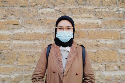 Portrait of young woman standing against brick wall