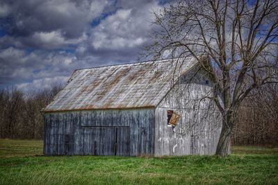 Weathered barn on field against cloudy sky